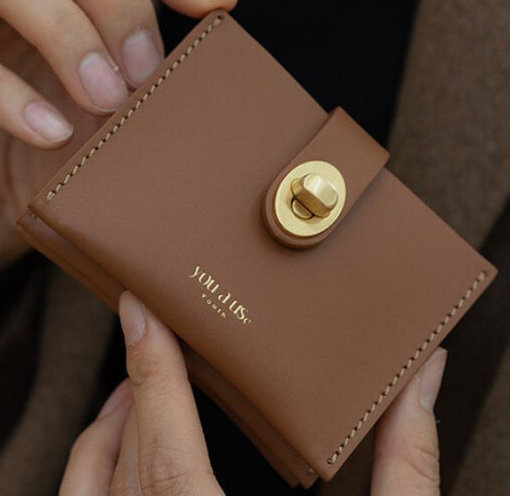 Brown leather wallet with gold clasp held by hands, brand 'Yohji Yamamoto' visible.