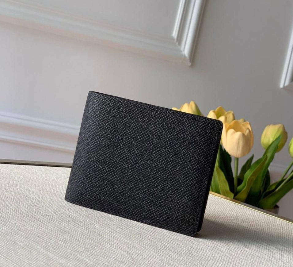 Black wallet on a light surface with yellow tulips in the background